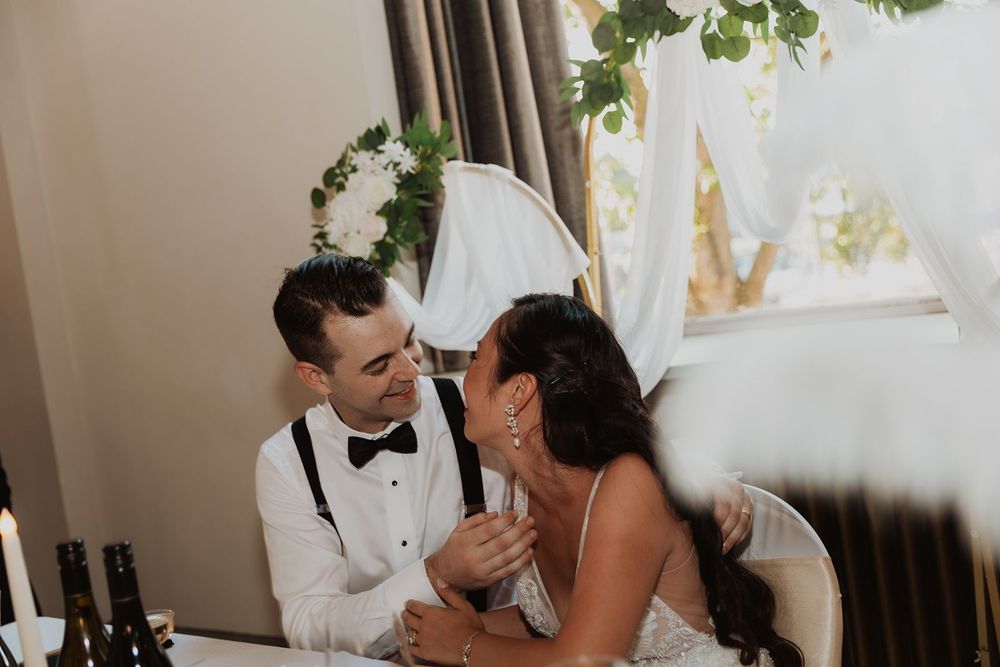 Bride and groom sharing an intimate moment at the sweetheart table during wedding reception.