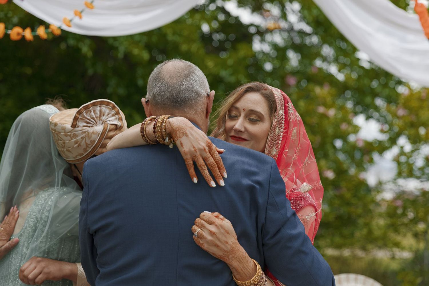 Family members sharing warm embrace during emotional outdoor Indian wedding ceremony celebration.