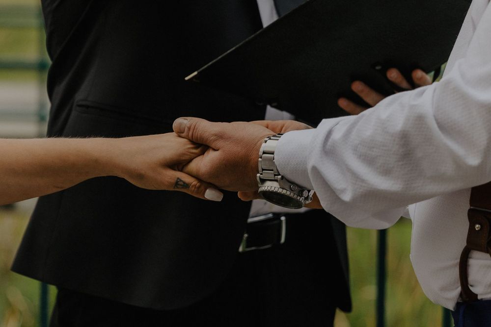 An officiant holds the hands of a bride and groom during a wedding ceremony ring exchange.