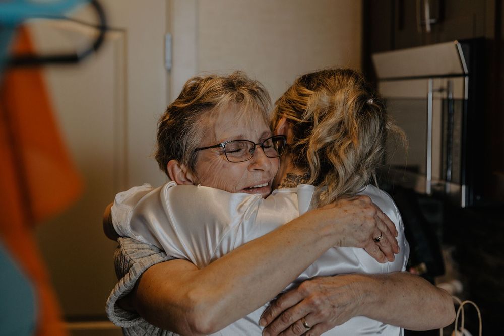 Two women share a warm emotional hug indoors on a wedding day.