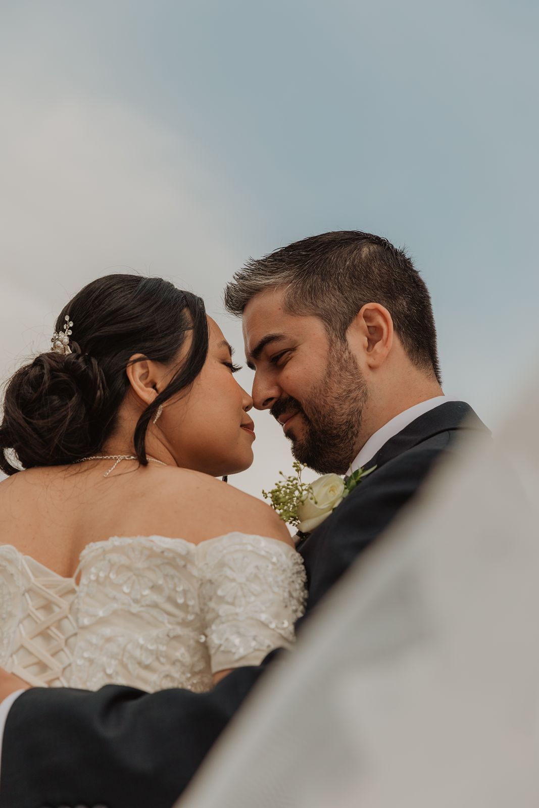 Bride and groom touching foreheads romantically under blue sky captured from low angle.