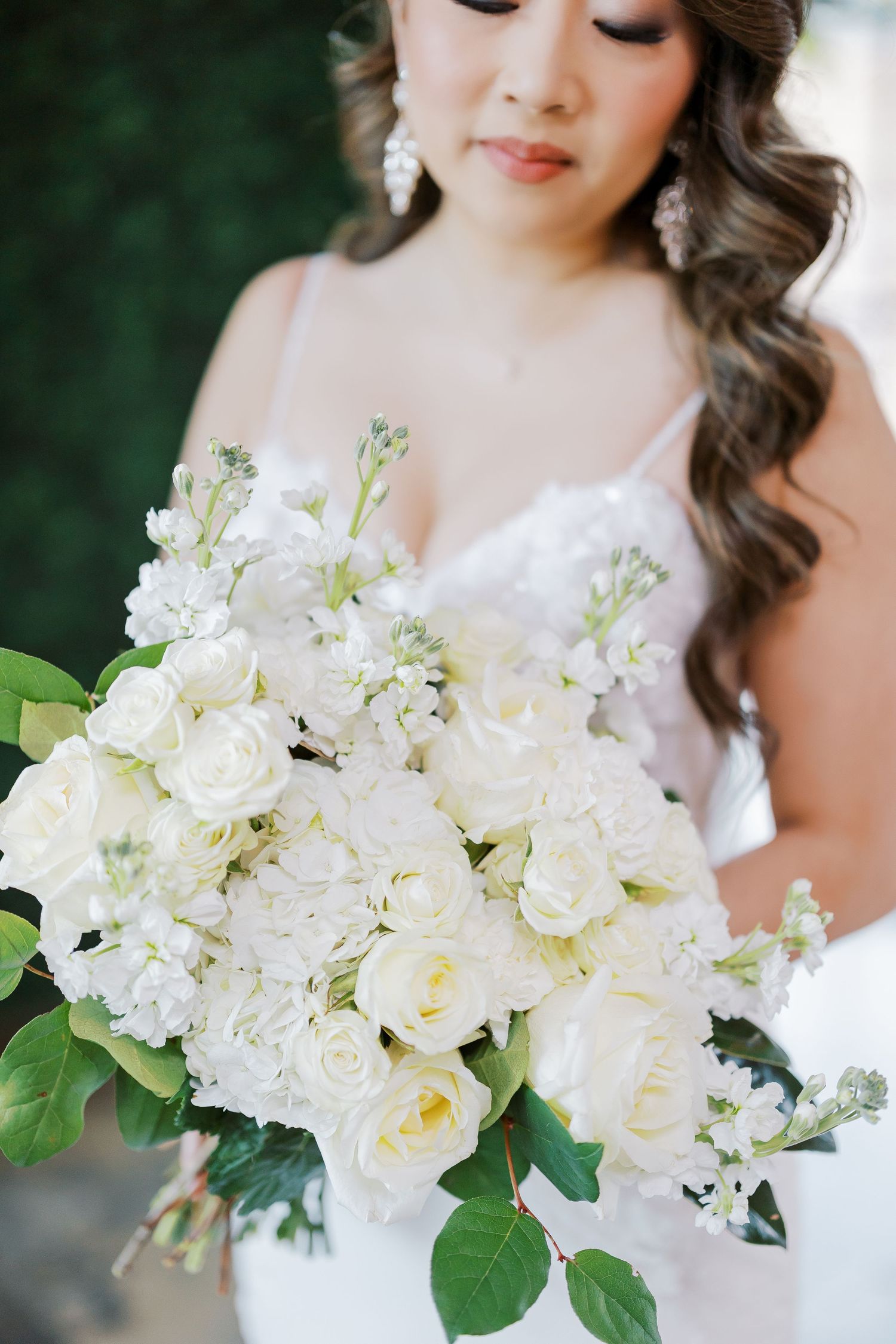 Beautiful white bridal bouquet with roses and mixed flowers against a blurred green background.