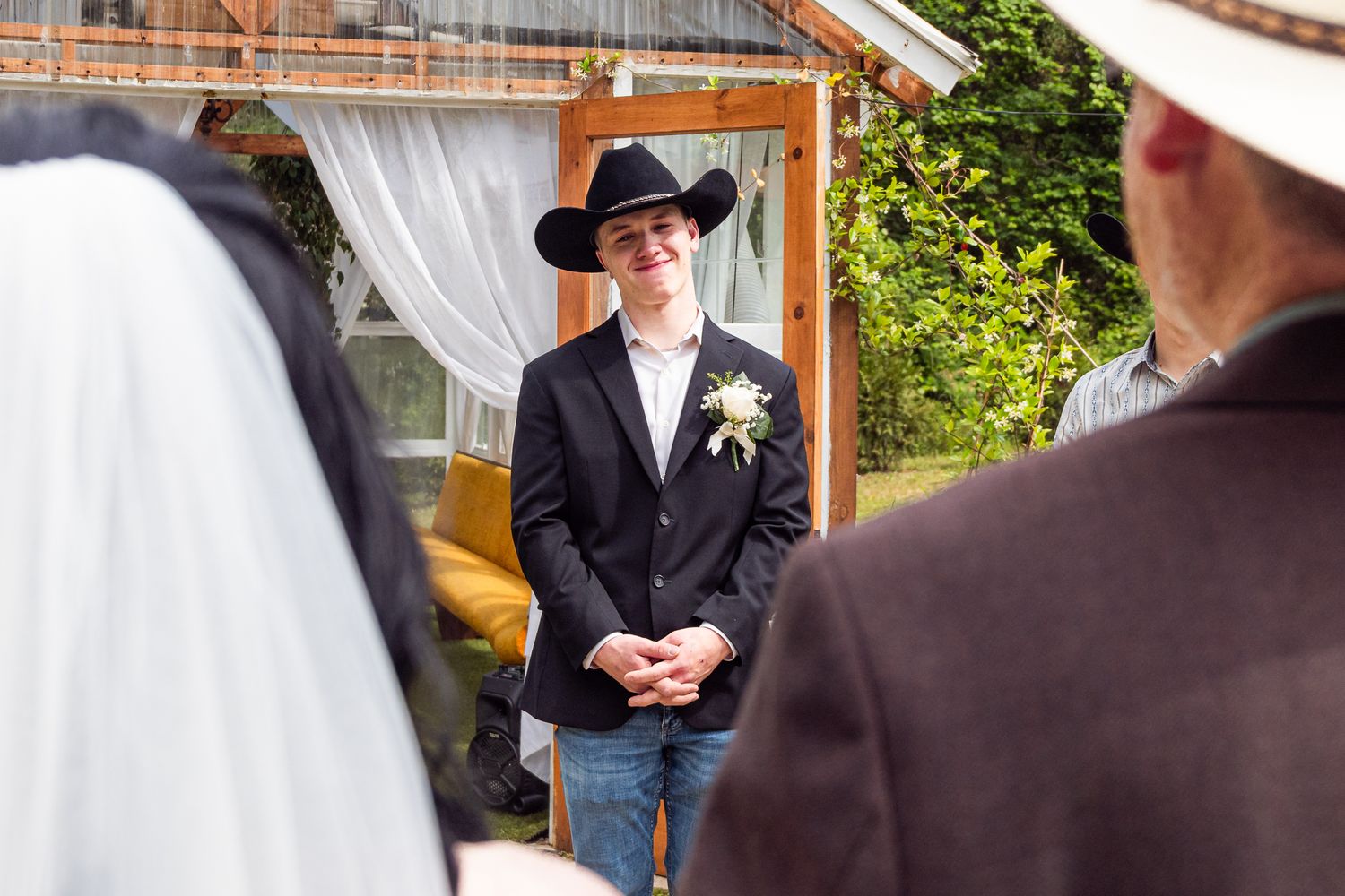 Wedding ceremony participants stand under a rustic wooden arch decorated with white fabric and floral arrangements.