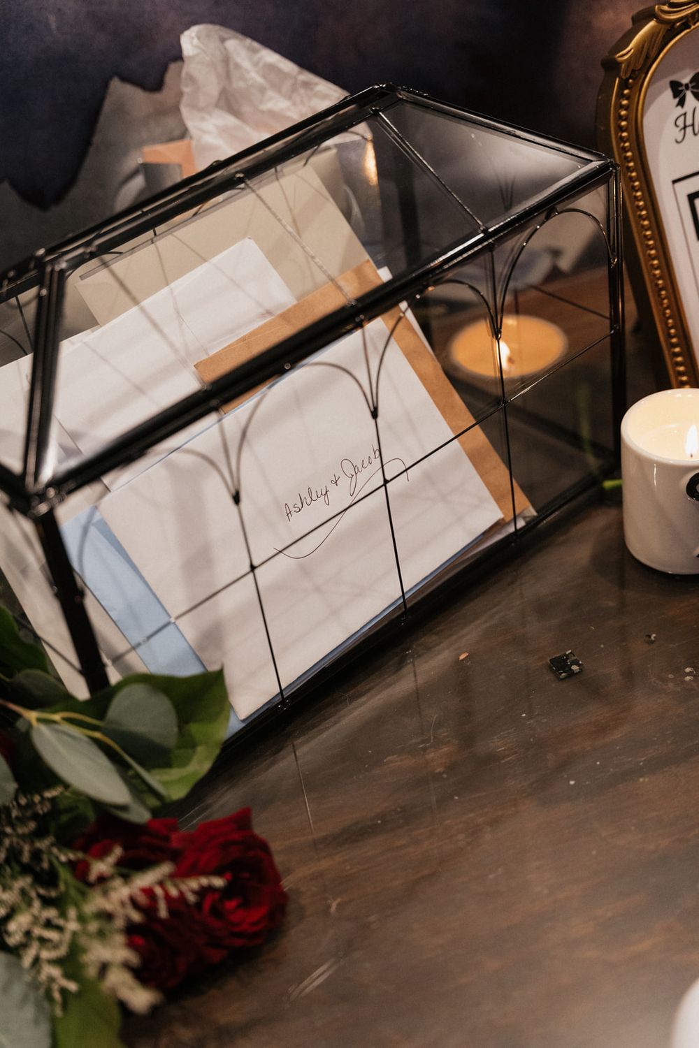 Wedding guest book and red roses displayed on dark wooden table with ambient lighting.