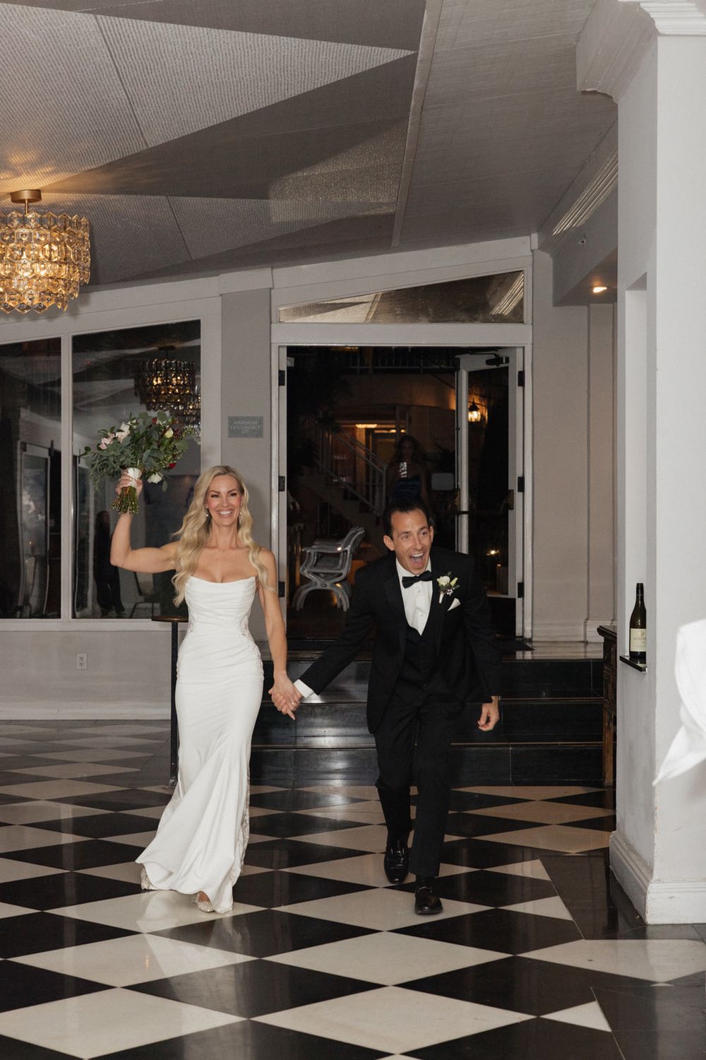 A wedding couple dances on a black and white checkered floor in an elegant reception venue.