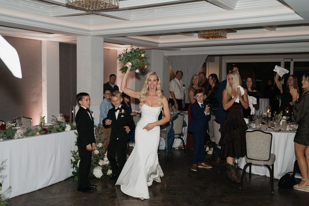 Wedding reception celebration in an elegant ballroom with guests gathered around decorated tables and white linens.