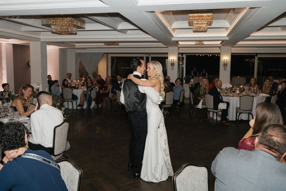 Wedding guests dance and celebrate on a dimly lit ballroom dance floor during an evening reception.