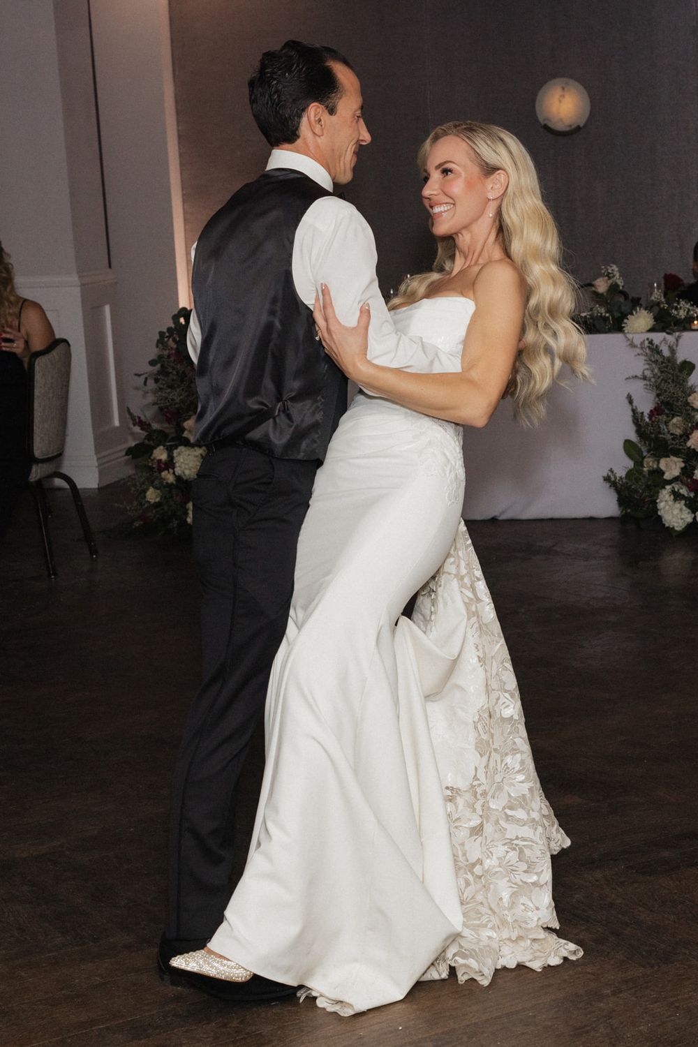 A couple shares their first dance at their wedding reception, with the bride wearing an elegant white gown with lace details.