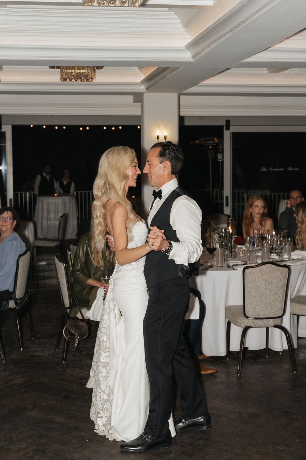 A couple shares a romantic dance together at a wedding reception in an elegant indoor venue with white tablecloths.