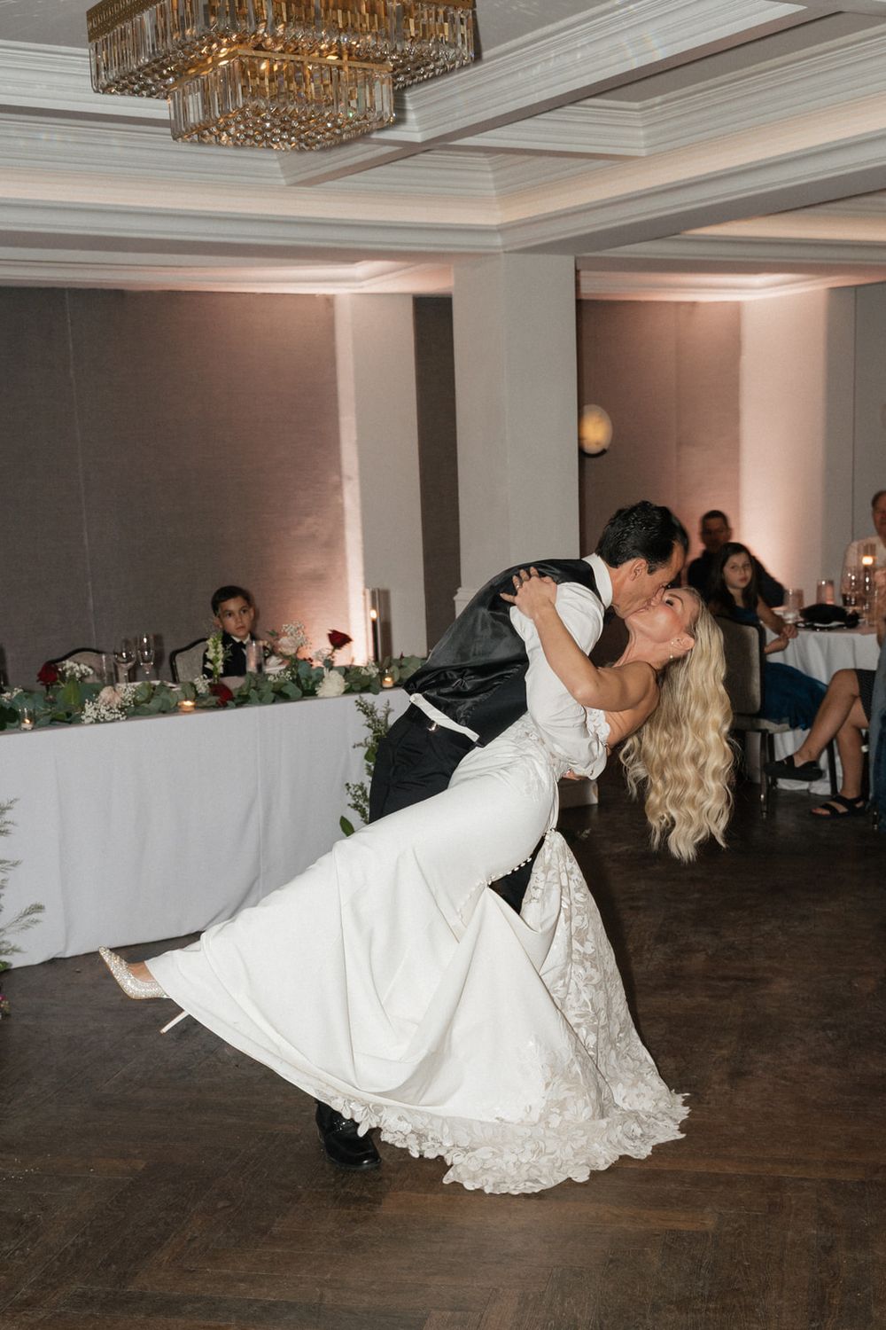 A romantic wedding dance dip sequence showing a couple in white formal attire on a wooden ballroom floor.