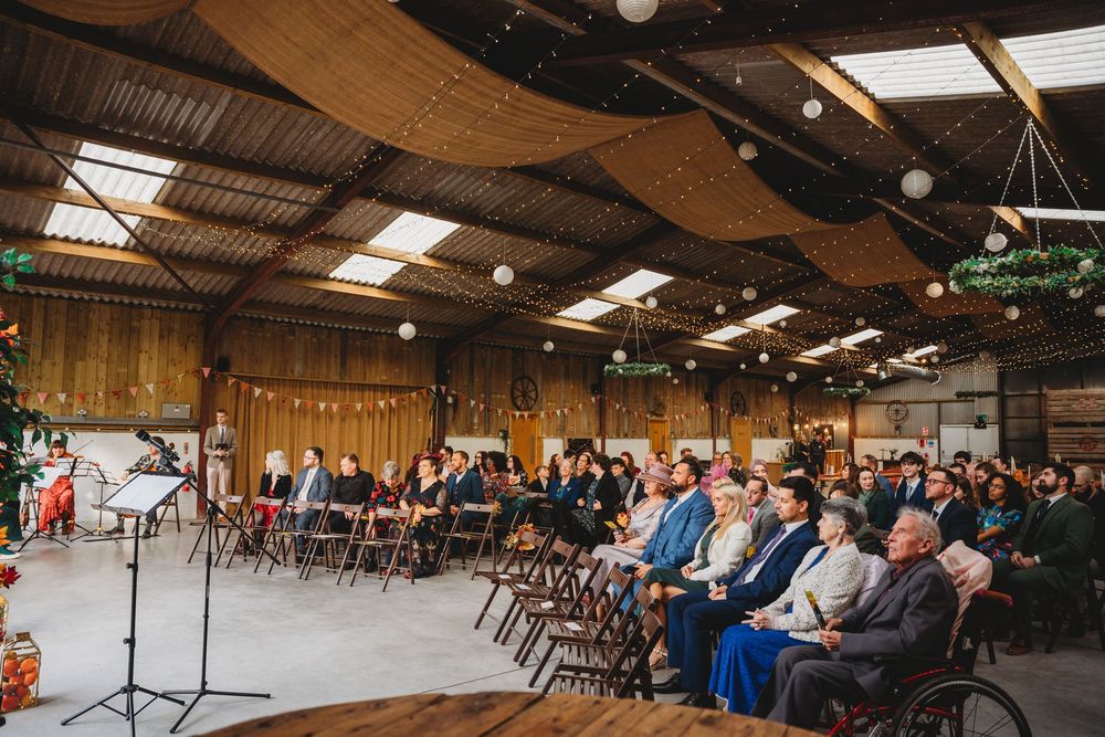 Wedding guests seated in rows inside a rustic barn venue with wooden walls and skylights overhead.