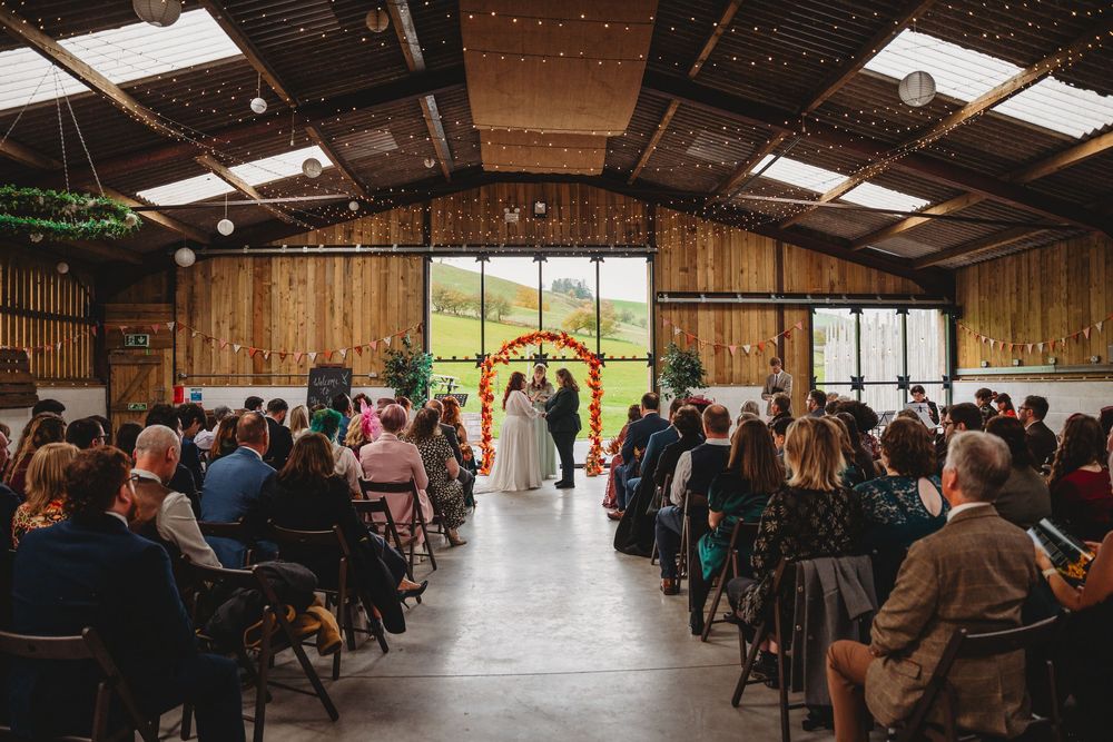 Long view of rustic barn venue interior with rows of chairs and natural lighting.