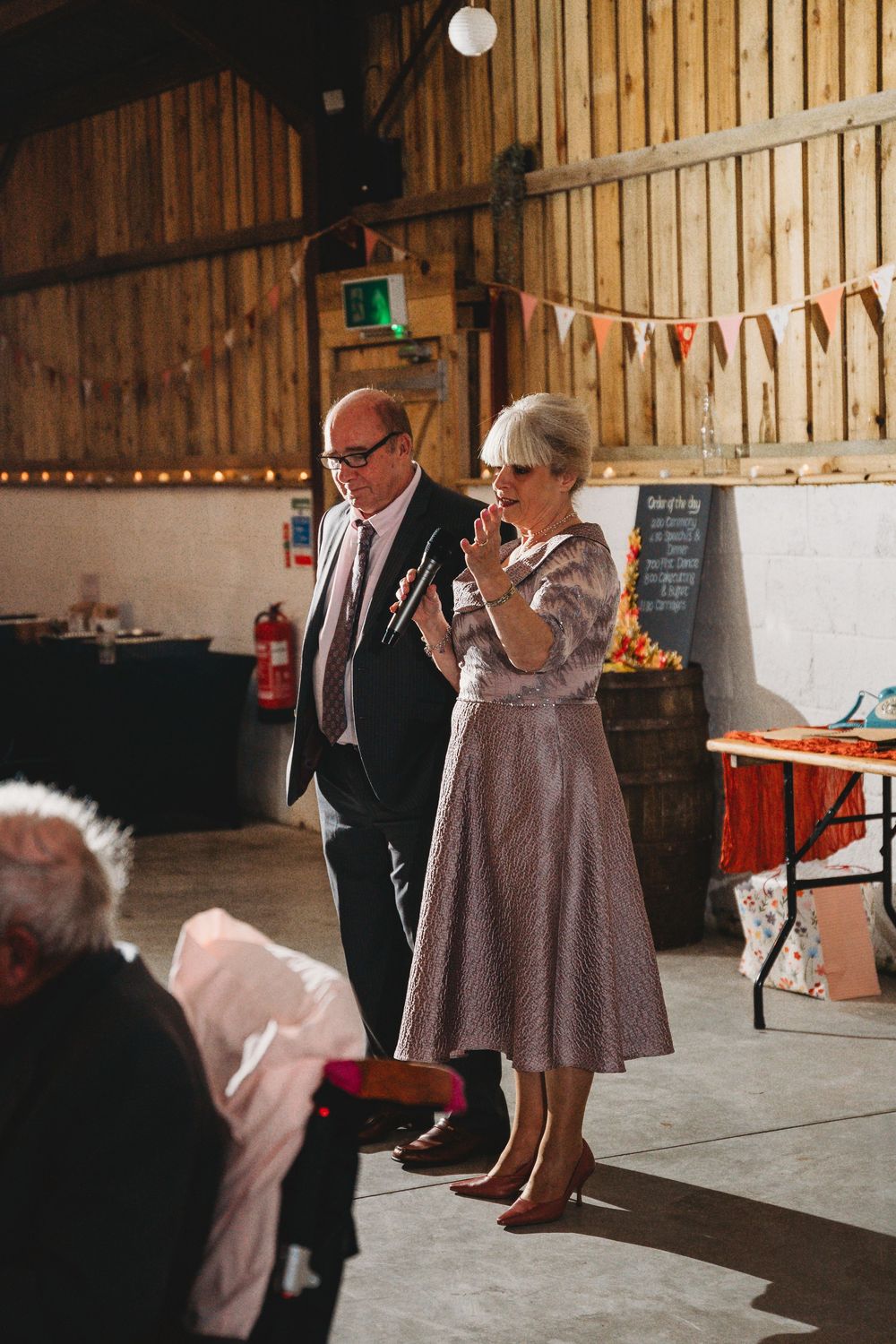 People dancing together in a rustic barn setting with wooden walls and string lights.