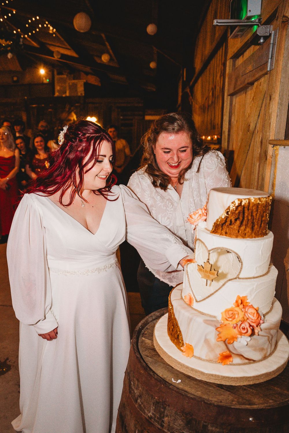 Beautiful white wedding cake with orange floral decorations being cut at a rustic reception.
