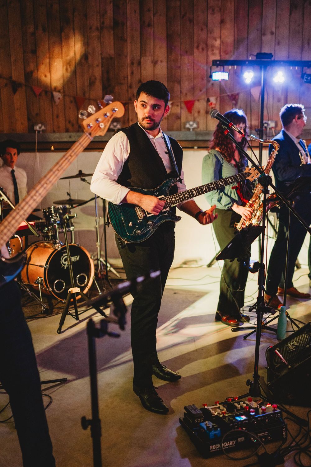 Live band performs with guitars and instruments on stage at a wedding reception in a wooden barn venue.