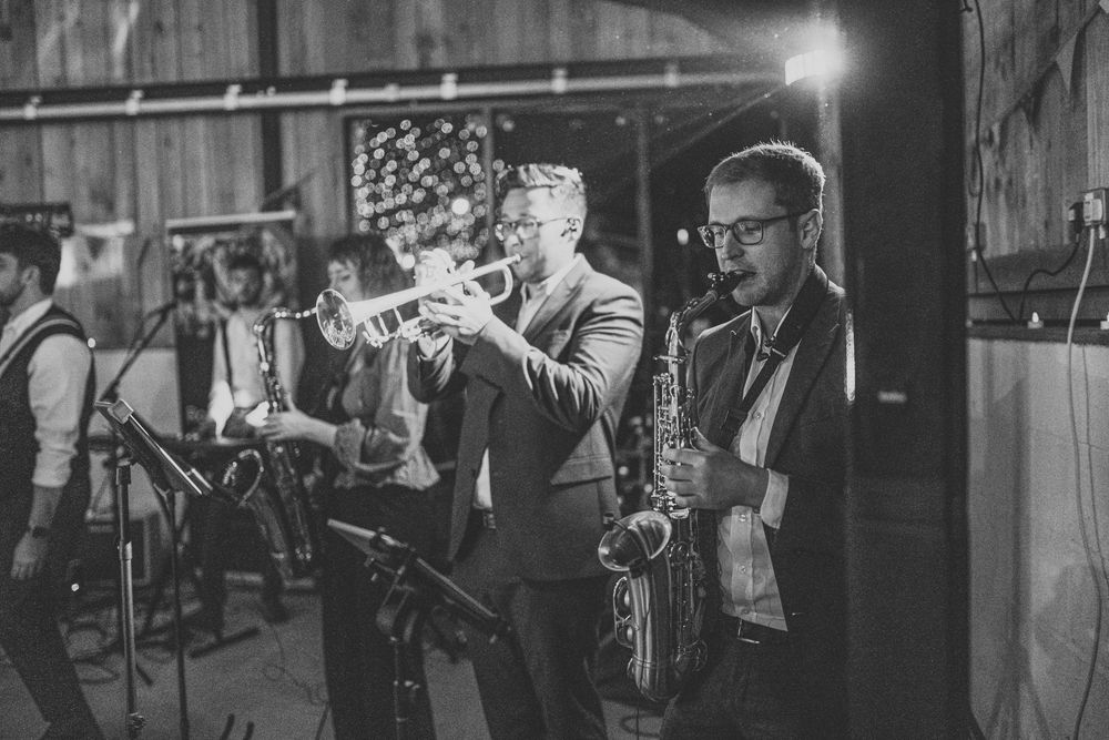 A band performs on stage with brass instruments in a dimly lit venue.