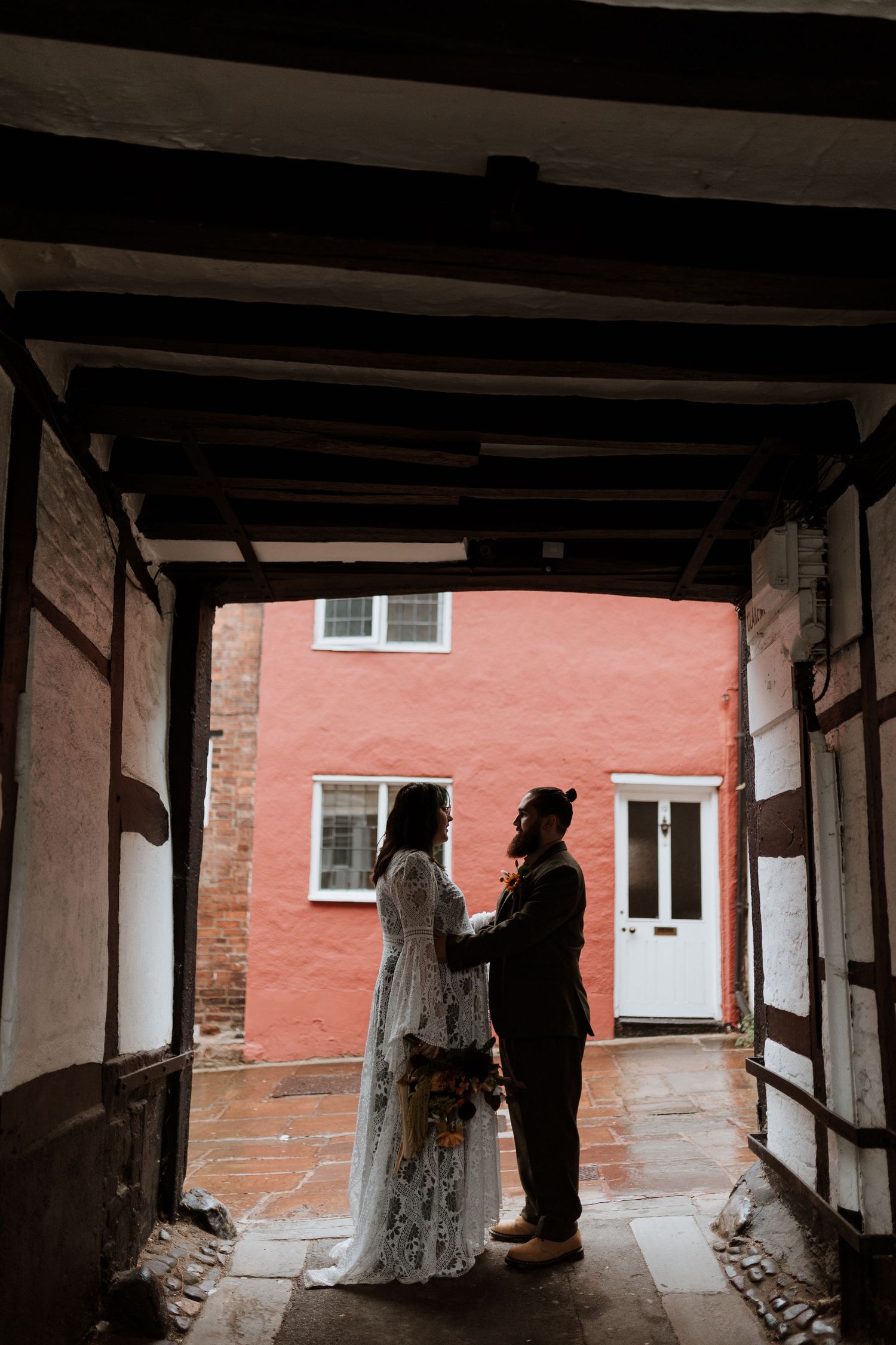 Silhouetted wedding couple standing in a dark passageway against a coral-colored building exterior.