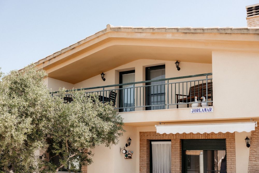 Modern beige stucco house exterior with balconies and American flag against blue sky.