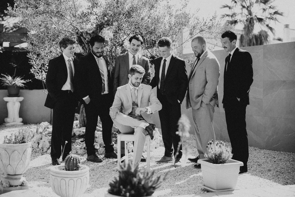 Black and white photo of a group in formal wear standing together outdoors with plants in the background.