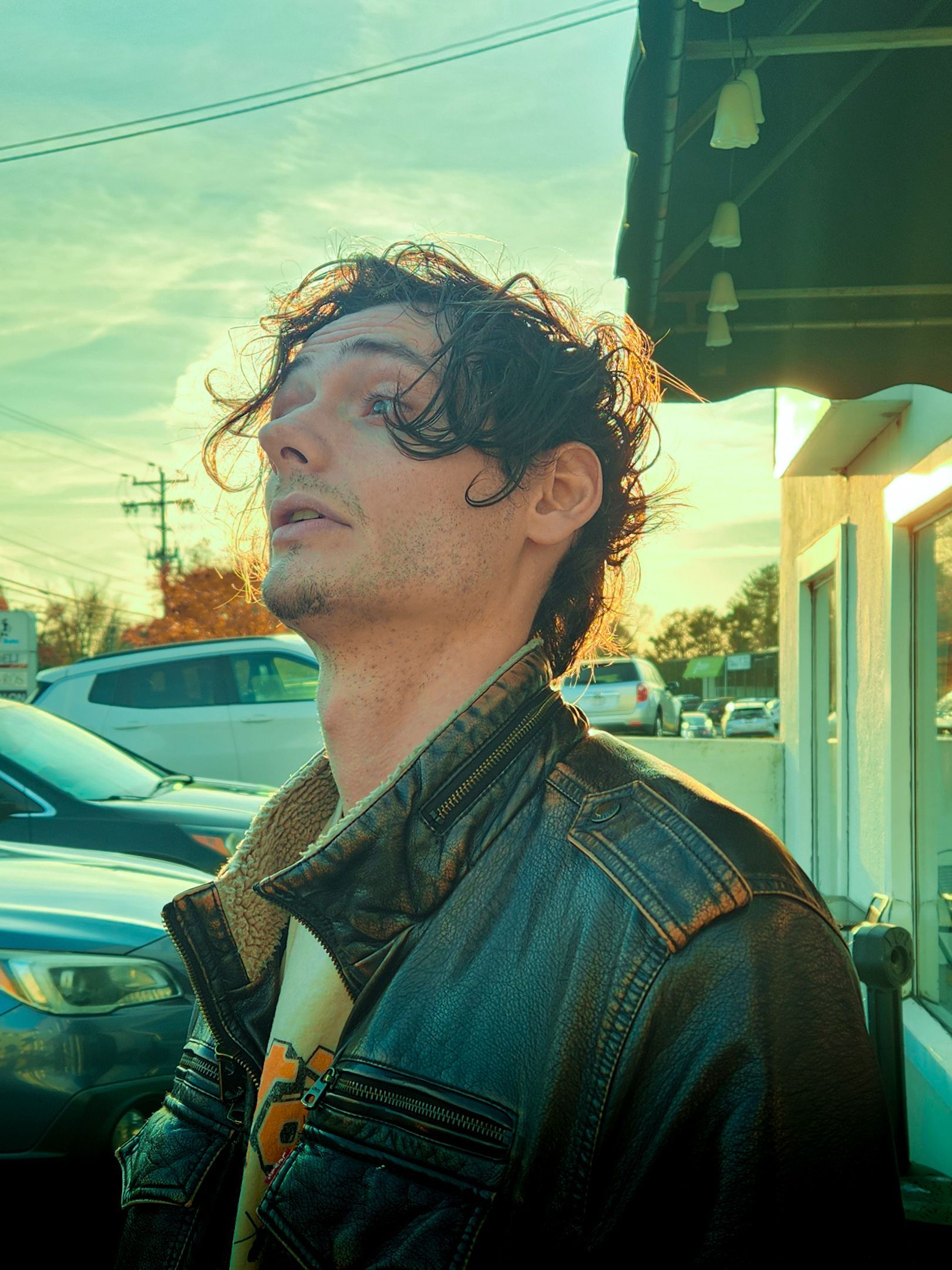 Person wearing denim jacket looking up at sunset sky with urban buildings in background.