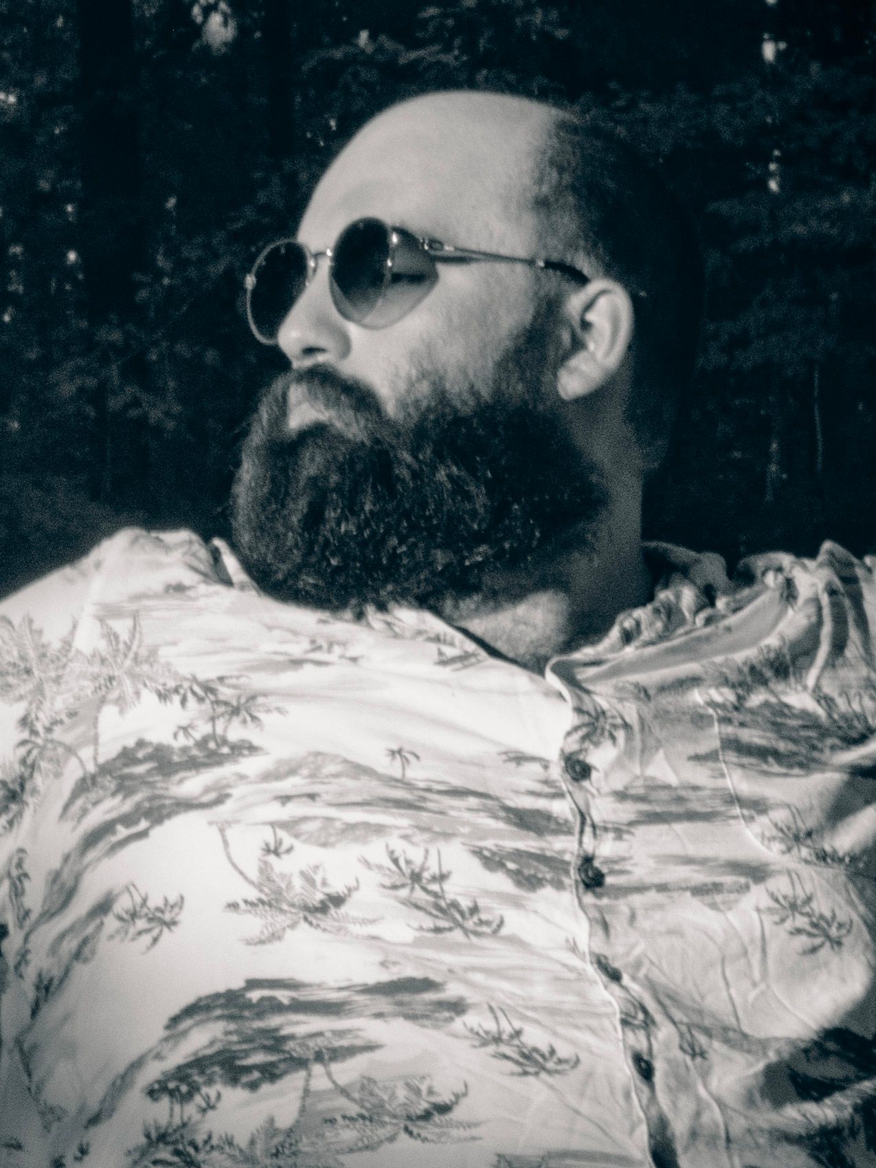 Person with sunglasses and beard rests on floral patterned fabric in black and white.