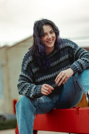 Person in dark sweater relaxing on red bench with casual pose.