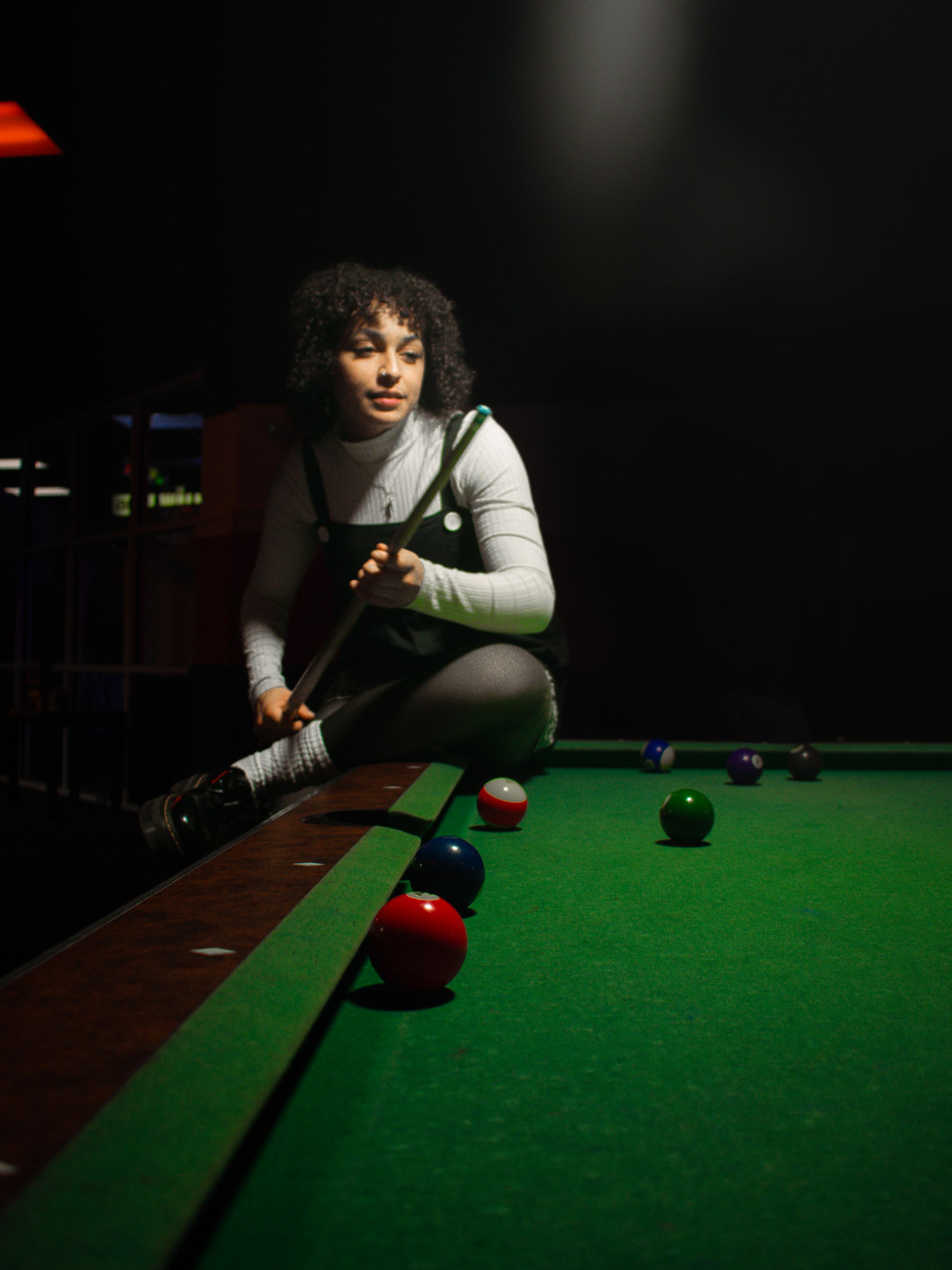 Player leans over green pool table in dramatic spotlight focusing on shot.