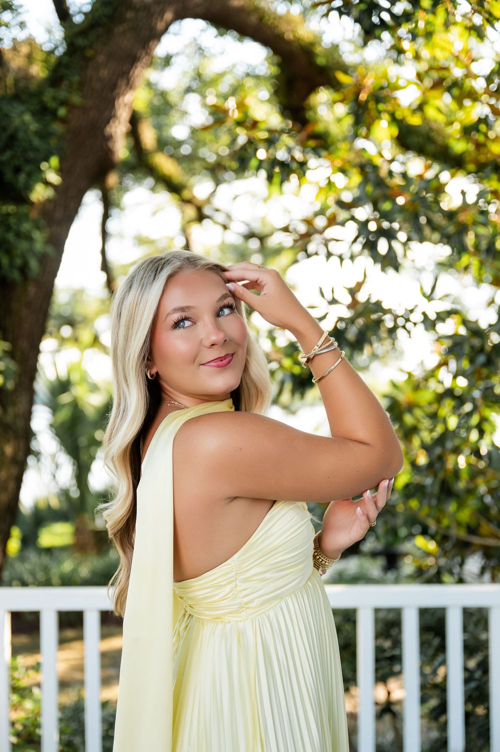 Ethereal yellow dress photographed on white railing deck with sunlit trees in background.