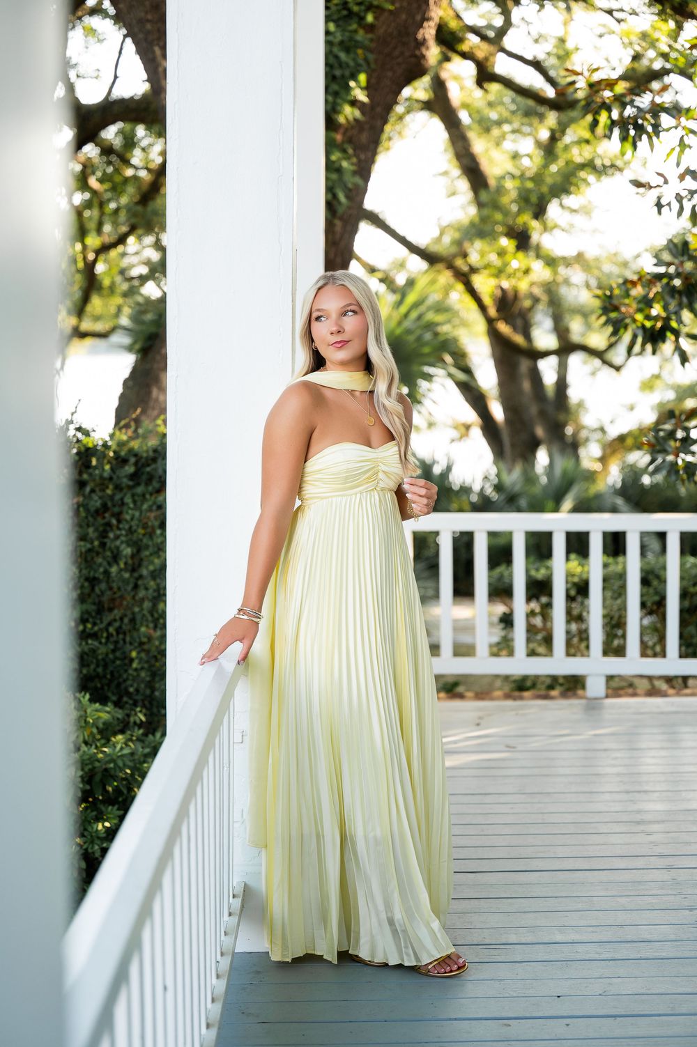 Pale yellow flowing dress styled on white porch with classic columns and greenery.