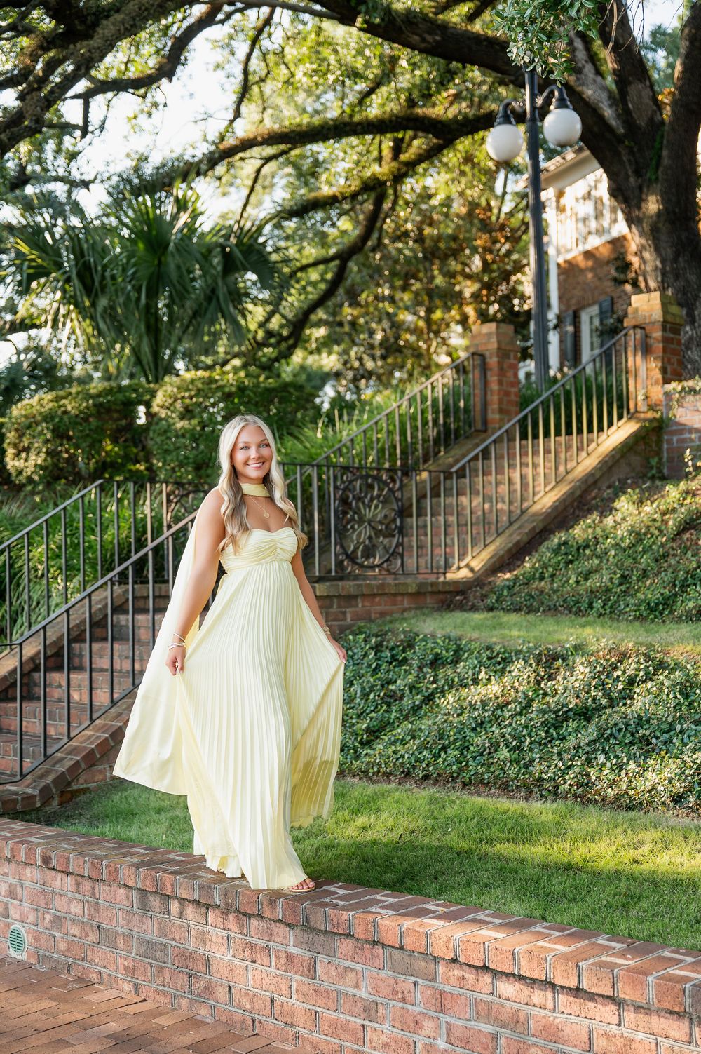 Yellow pleated dress photographed on brick steps with wrought iron railing and garden setting.