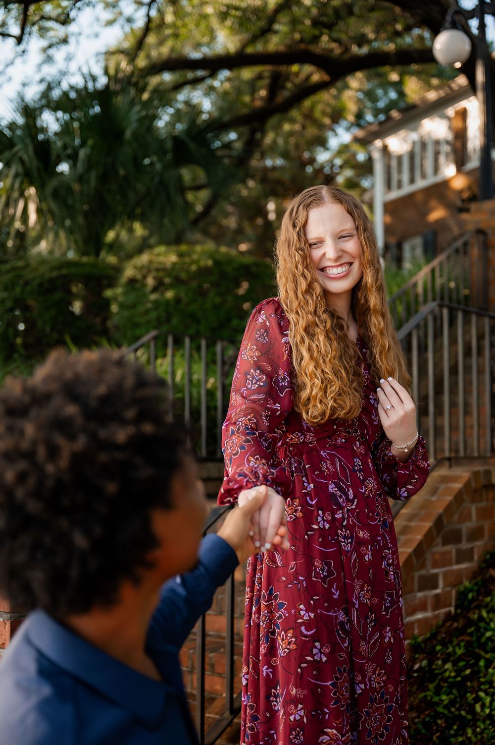 A couple shares joyful moments along a brick wall pathway outdoors.