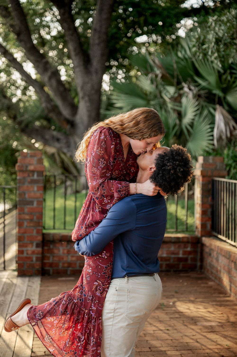 A couple embraces and dances on a brick patio surrounded by trees and greenery.