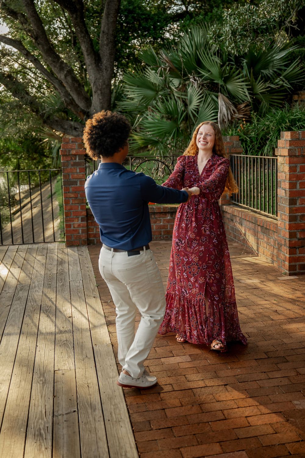 A couple dances playfully on a brick patio with garden views.