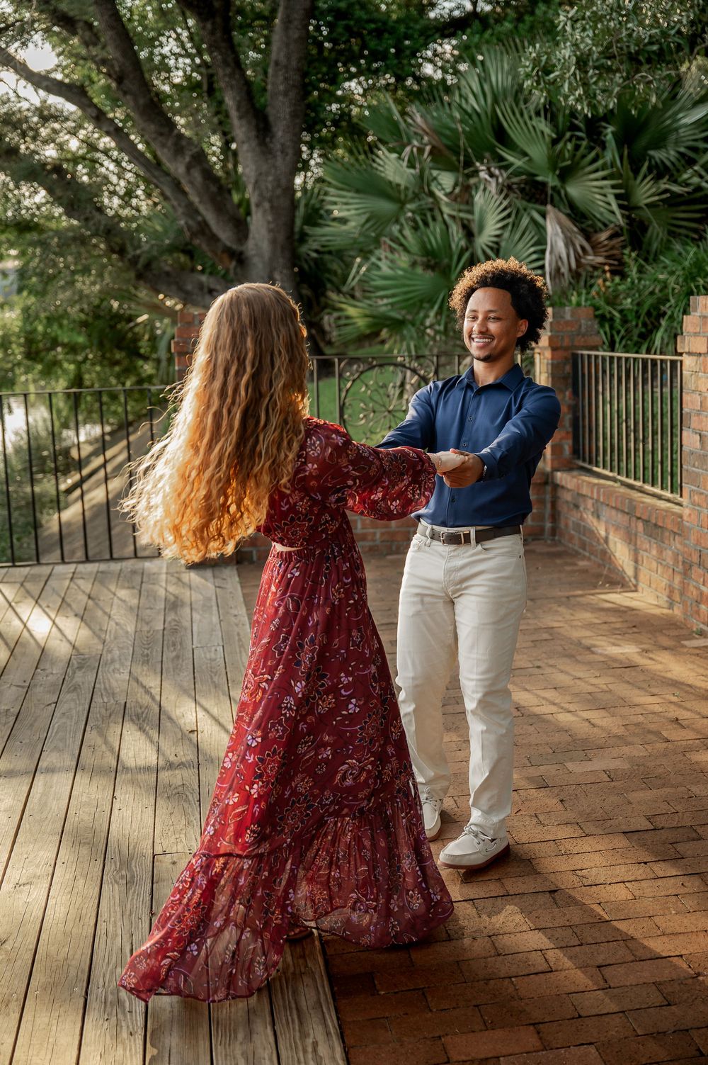 A couple spins and dances together on an outdoor brick patio.