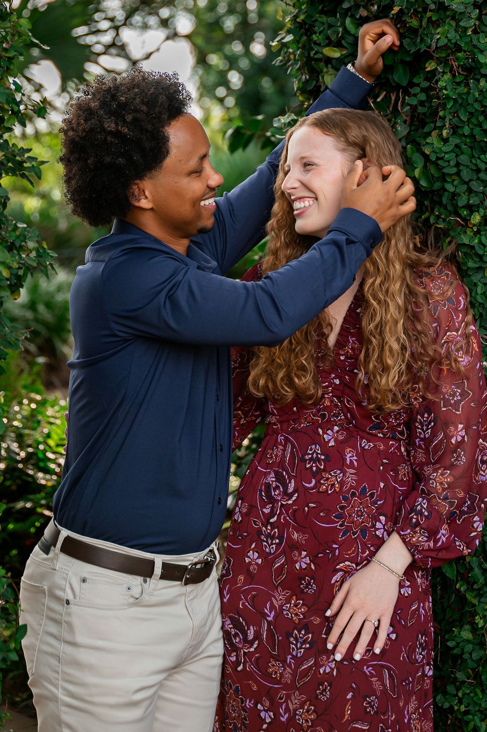 A couple shares an intimate moment among green foliage during a sunny afternoon.