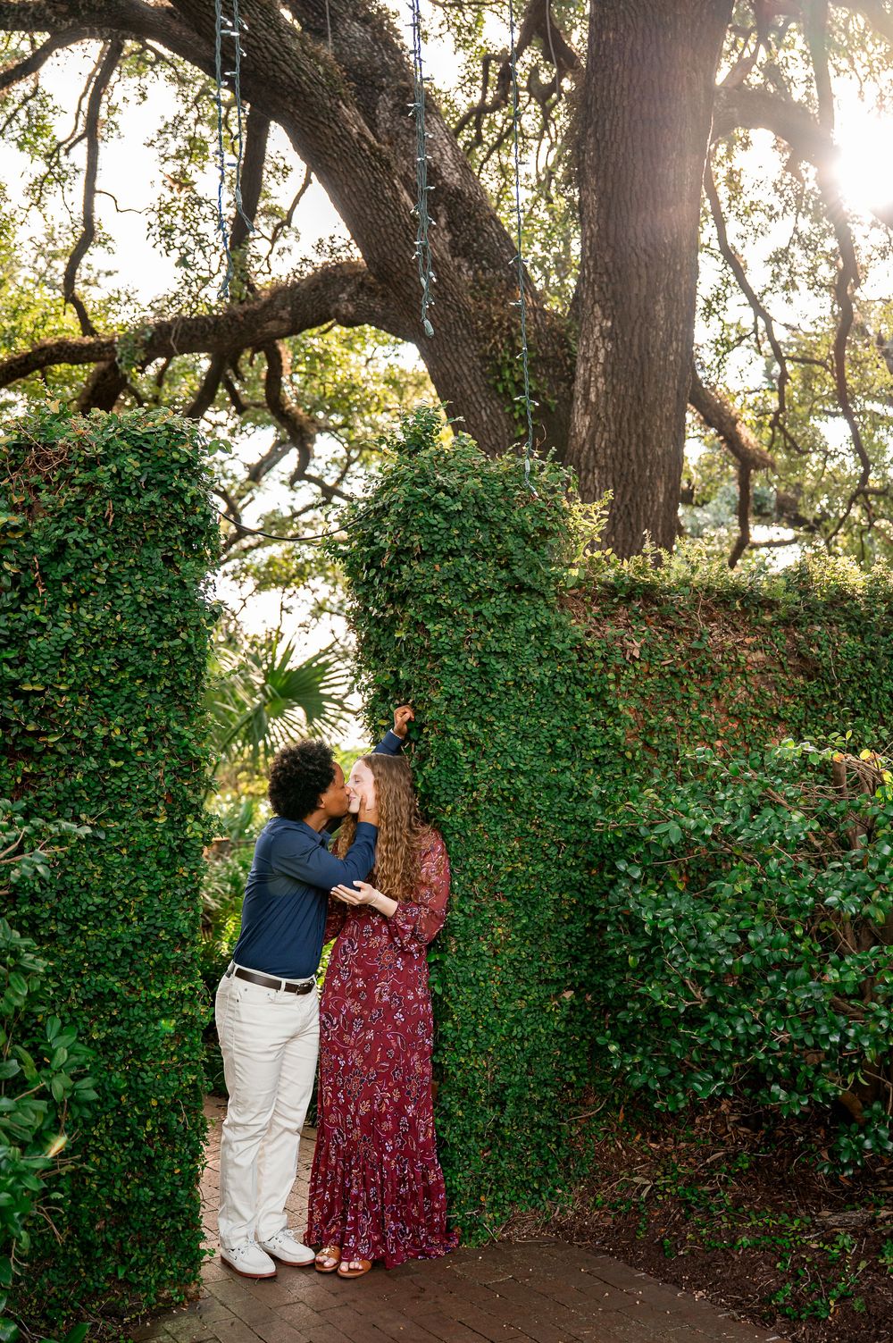A couple embraces near ivy-covered trees in a romantic garden setting.