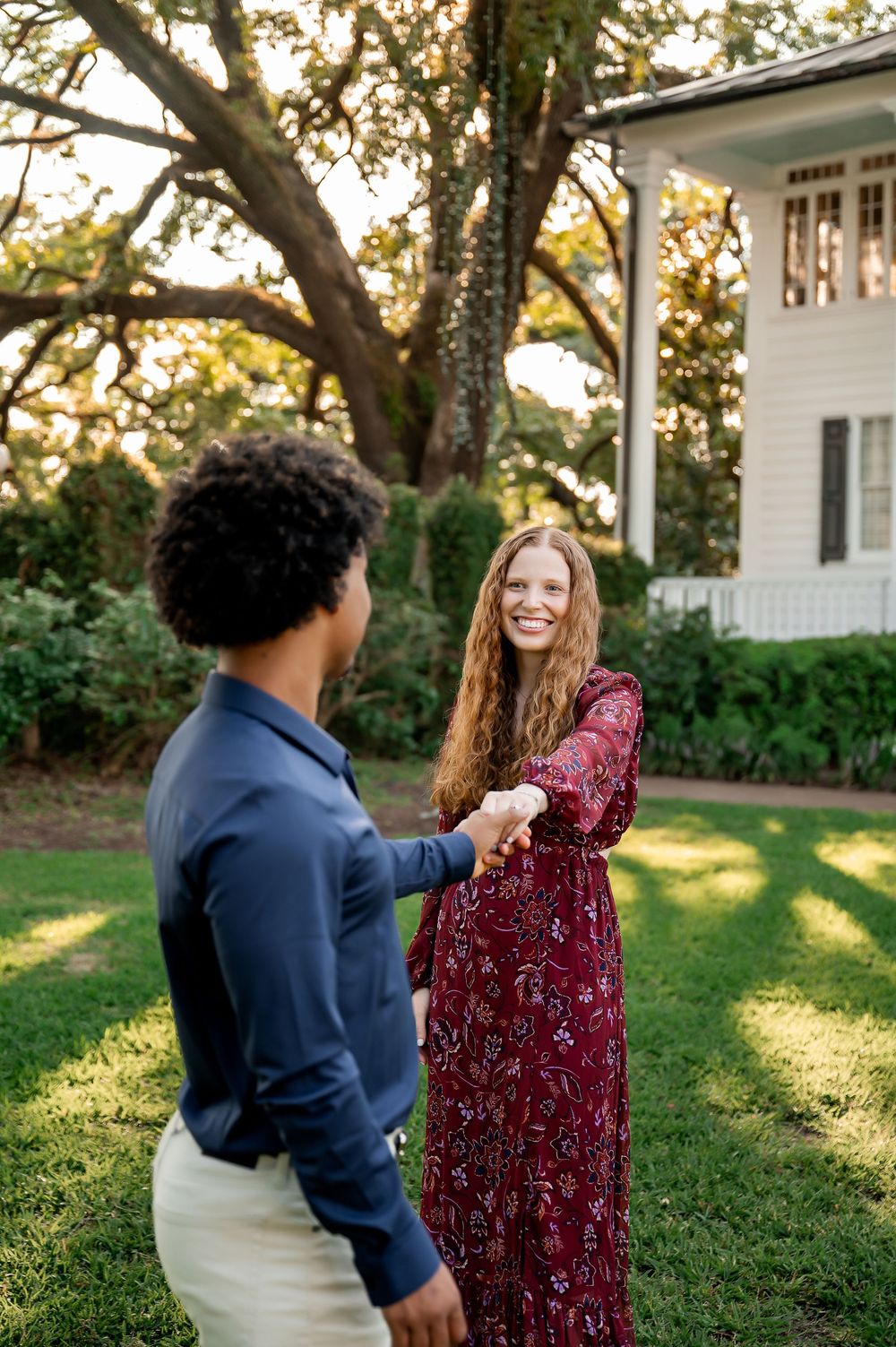 A couple shares a special moment on a lawn near a white house during golden hour.