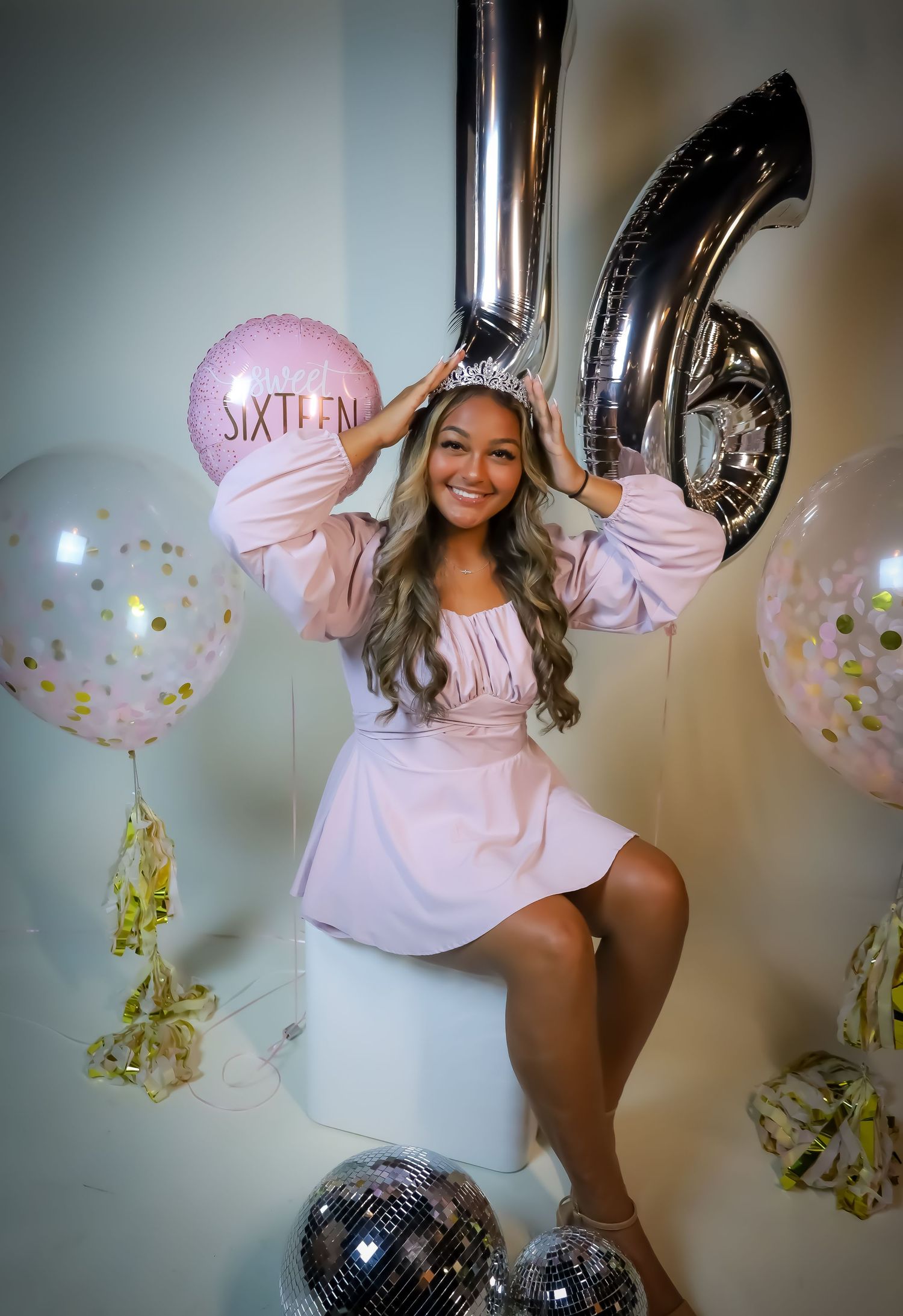 Sweet sixteen birthday celebration with pink and silver balloons against white wall.