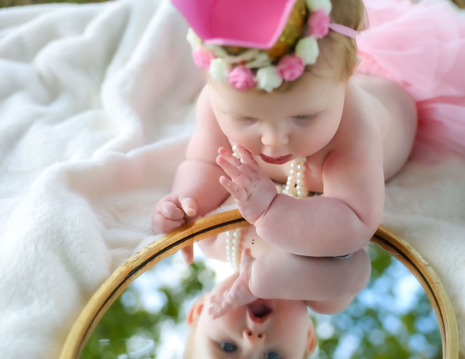 Baby wearing floral headband lying on soft white fabric in natural light.