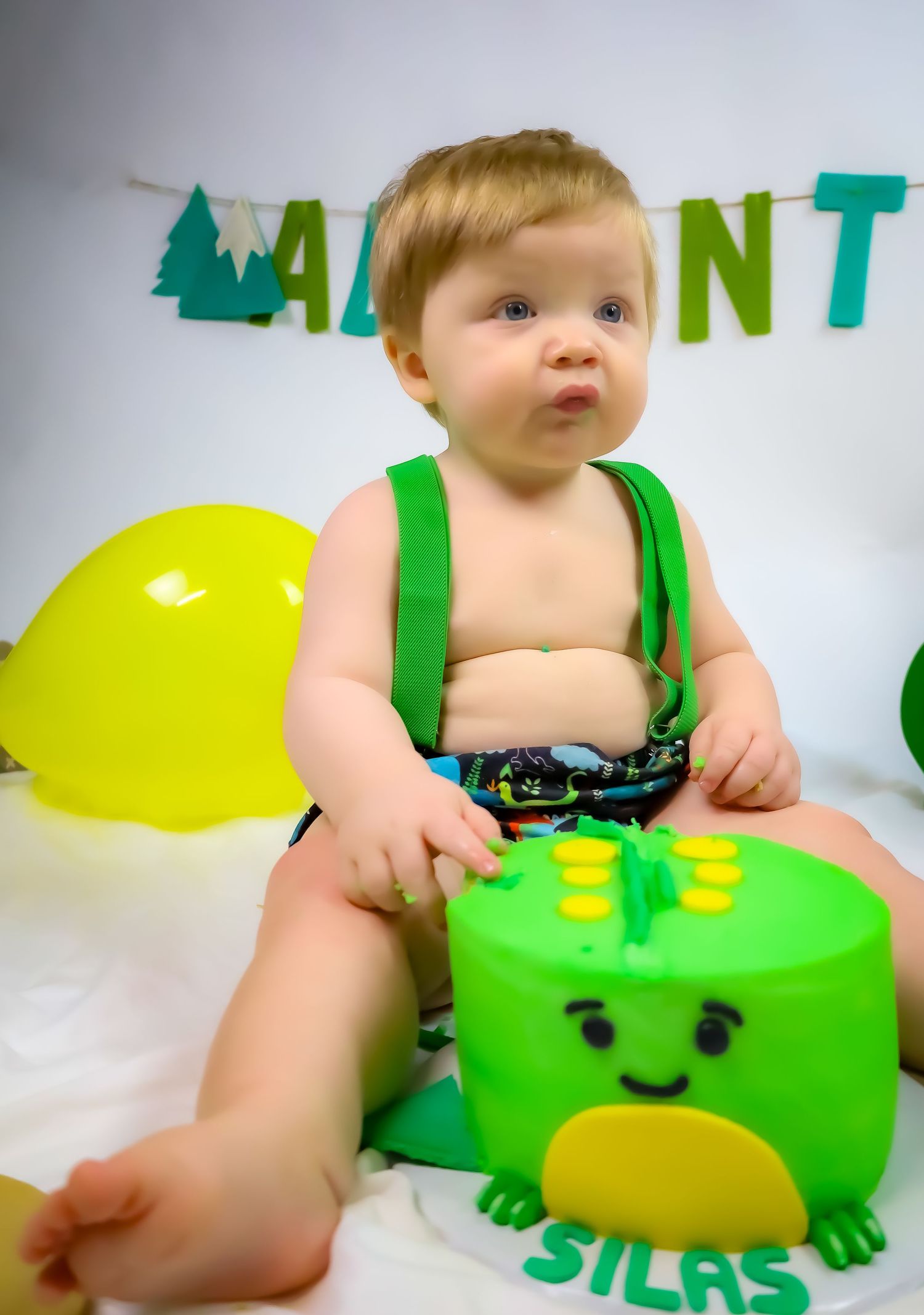 Green dinosaur-themed cake setup with yellow balloons and adventure banner.