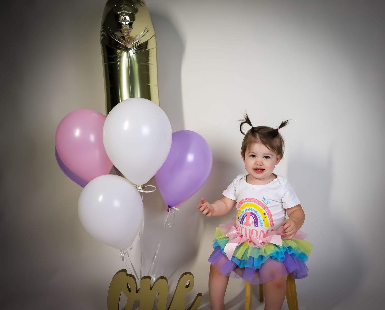 Birthday celebration setup with pastel balloons and cake against a white studio background.