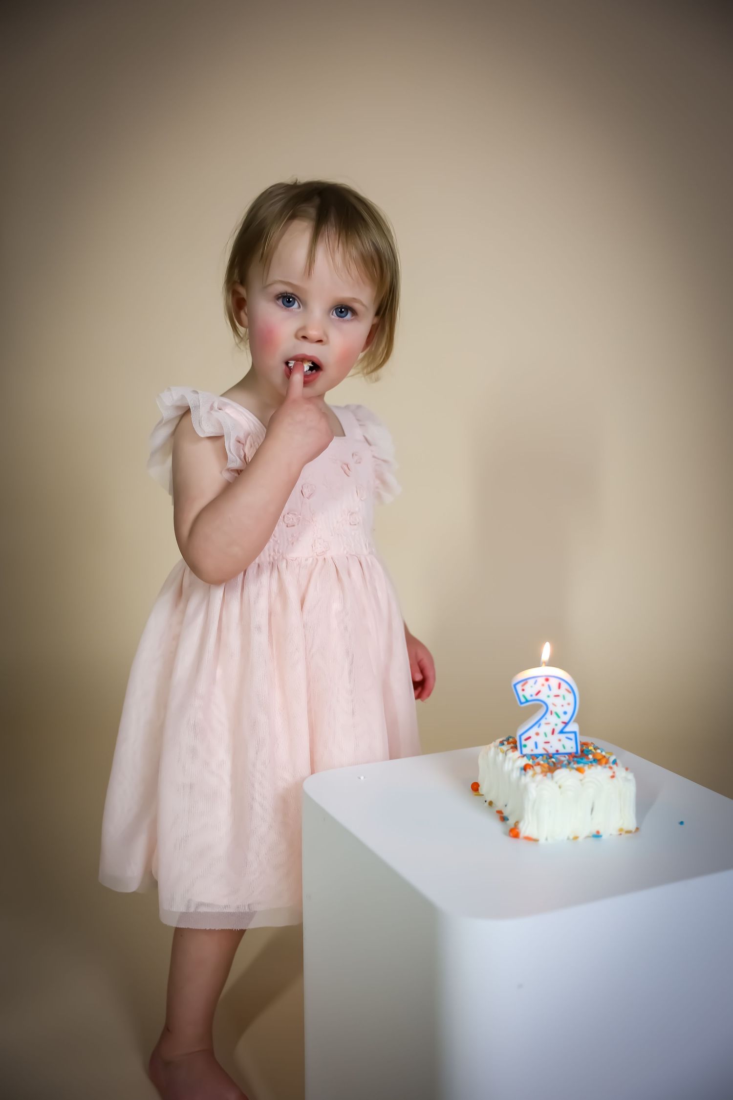 A small birthday celebration with a pink dress and number 2 candle on a white cake.