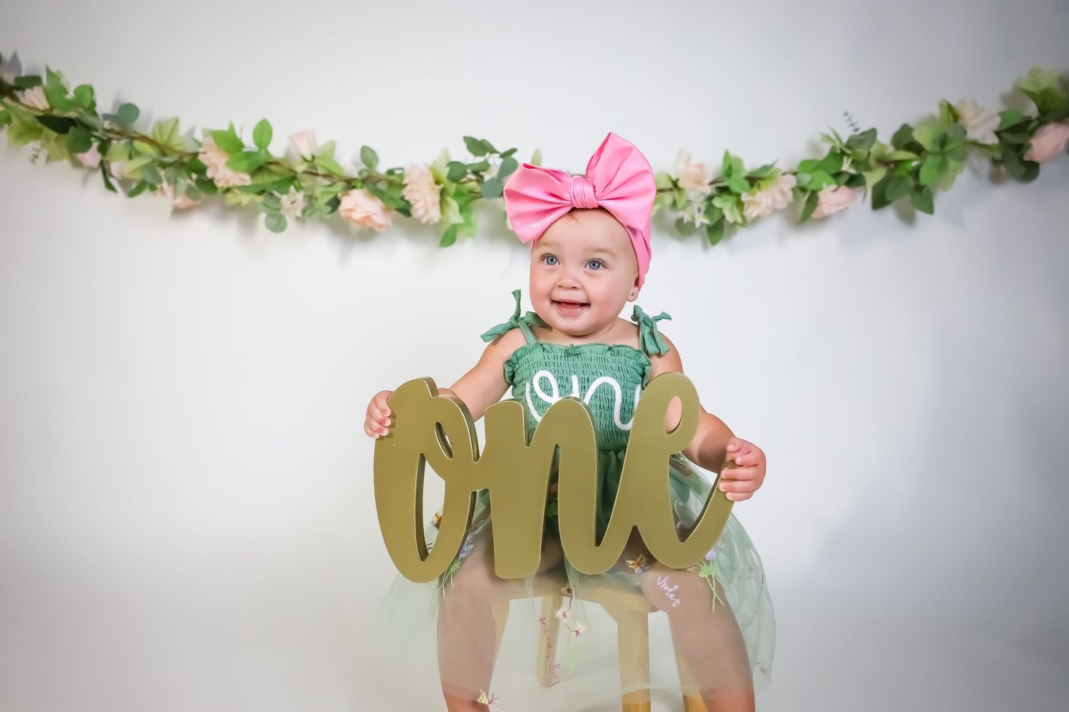 Birthday photo featuring mint tulle dress and gold 'one' sign against white backdrop.