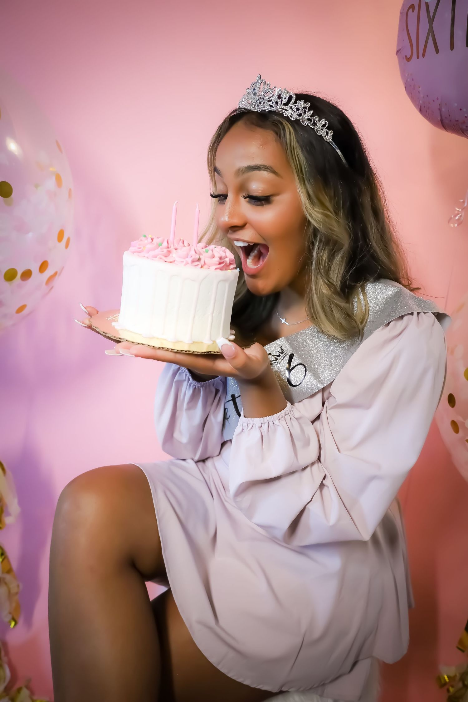 Birthday celebration with cake and tiara against pink backdrop.