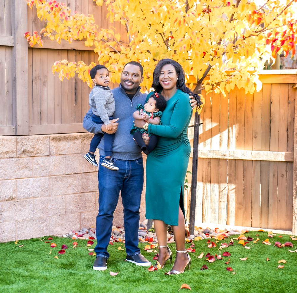 A family stands together in a backyard with vibrant fall foliage and a wooden fence in the background.