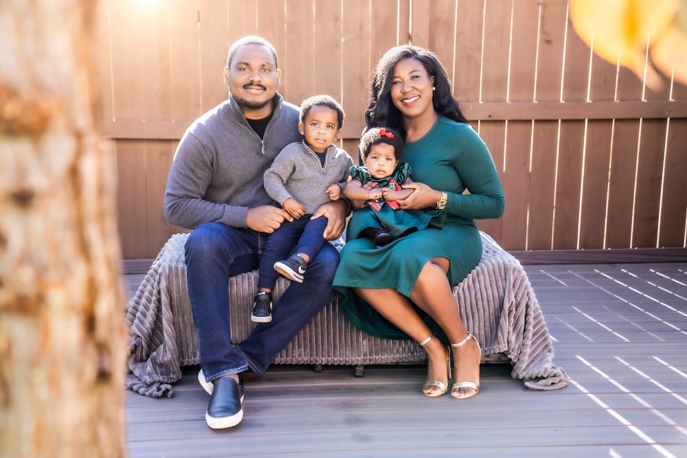 A family sits together on a bench outdoors, wearing coordinated outfits in blue and green tones.