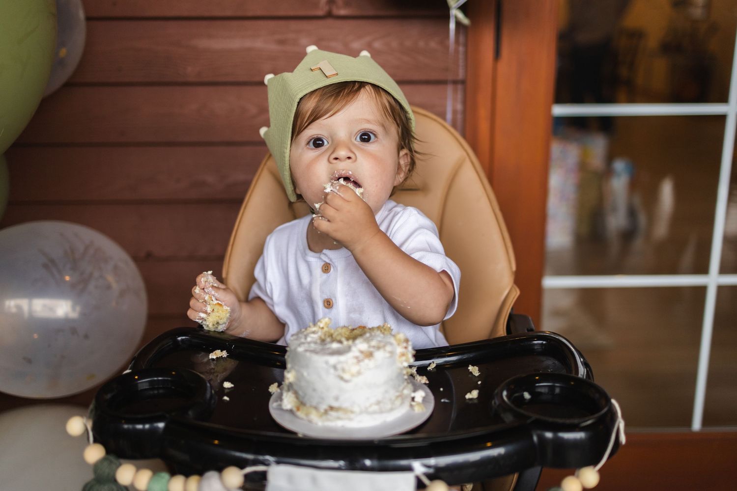 A toddler in a high chair reaches for food while making a silly face during mealtime.