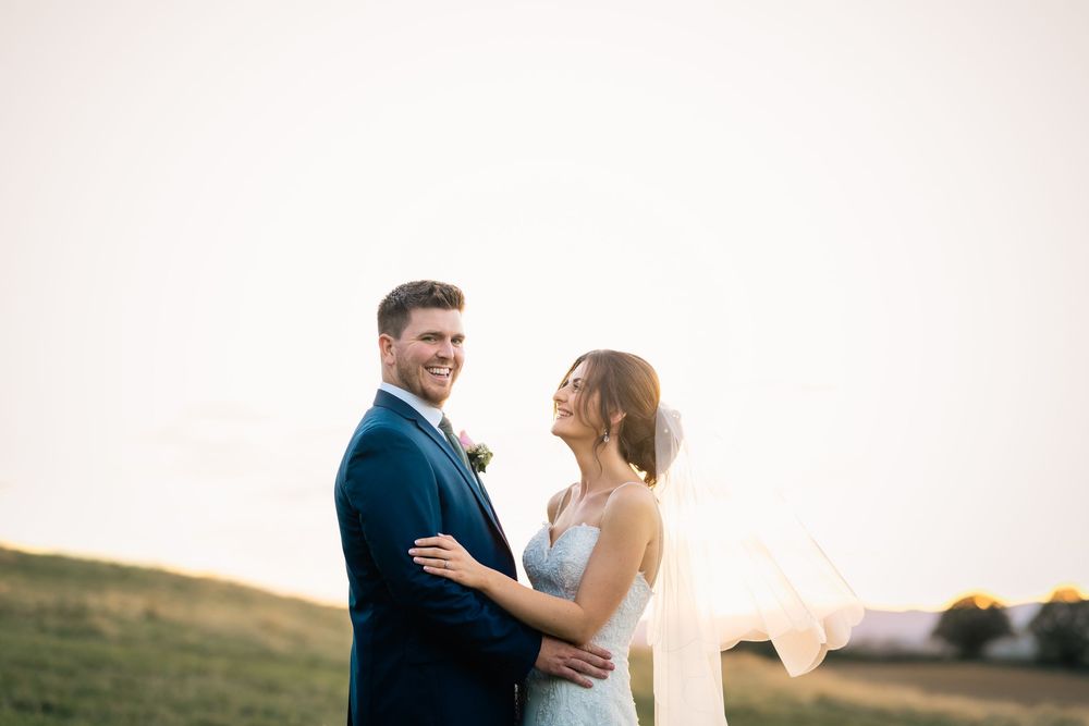 A couple embraces during a romantic sunset photoshoot in an outdoor field setting.