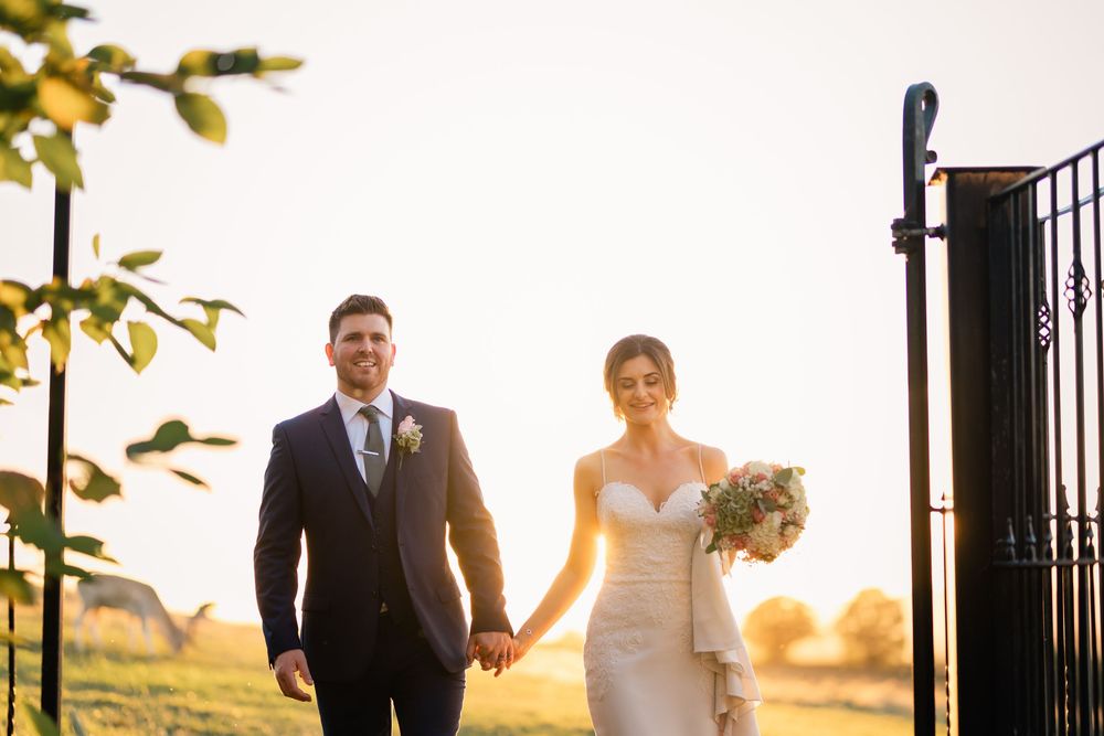 Newlywed couple walks together through a garden path during golden hour sunset lighting.