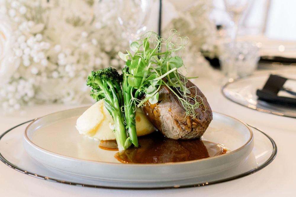 Elegant plated dish featuring seared meat with green garnish and creamy sauce on a modern white plate.